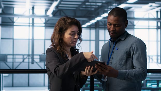 Computer scientists in data center using tablet to develop disaster recovery plans. IT professionals in server farm discussing, testing failover scenarios, protecting data during disruptions, camera A