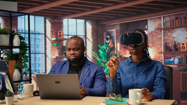 Black people integrate VR and AI into their daily job routine where the man engages in immersive 3D experience. Young focused woman reviews the animation on headset within the metaverse. Camera A.