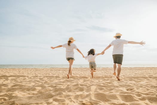 Happy Asian parents with their daughters enjoying playful at beach. Little girls with their mother and father holding hand of child running and pretending on sand. Positive family outdoor activity