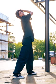 A woman stands confidently outdoors in comfortable attire, with the sunlight casting a warm glow. The background features construction scaffolding and greenery, creating a vibrant atmosphere.
