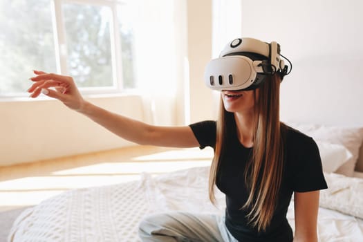 A young woman enjoys a virtual reality experience in a well-lit bedroom. She wears a VR headset and interacts joyfully with the digital environment, creating a lively atmosphere.