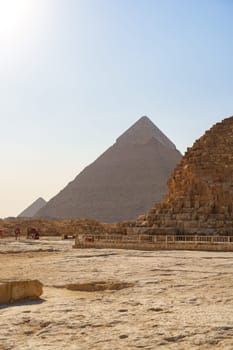 Tourists explore the historic Giza pyramids, surrounded by sandy terrain and ancient stone structures, during a sunny day in Egypt. The iconic pyramids stand proudly against the horizon.