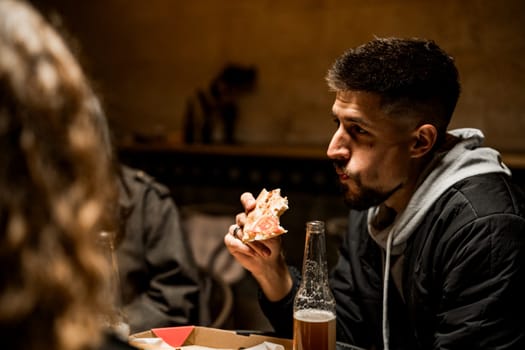 Two friends share a lighthearted moment in a warm restaurant while savoring pizza and drinks. The atmosphere is relaxed as they enjoy their meal and conversation.