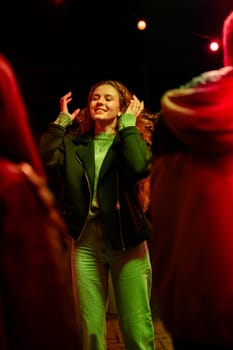 A young woman expresses joy as she dances at a vibrant outdoor event. Colorful lights illuminate the scene, creating a festive atmosphere as attendees socialize together.