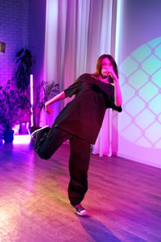 A dancer showcases their creativity in a lively studio filled with colorful lights. The performer is moving gracefully, wearing casual clothing and engaging with the energetic atmosphere.