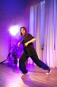 A dancer showcases a vibrant routine in a well-lit studio. The atmosphere is enhanced by colorful lights and flowing curtains, creating an engaging backdrop for the performance.