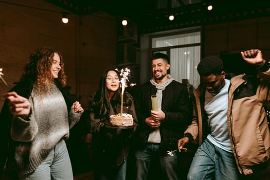 Friends gather to celebrate a birthday under string lights, holding sparklers and enjoying a cake. Laughter and joy fill the atmosphere as they dance together.