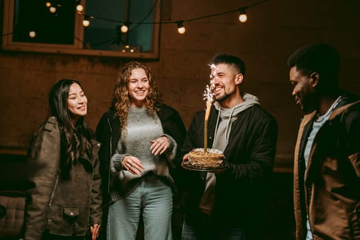 Group of friends gather outdoors at night to celebrate a birthday, sharing laughter and joy while enjoying cake topped with a sparkler. The atmosphere is festive and warm.
