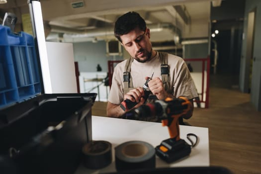A skilled worker adjusts his tools while seated at a well-organized workbench in a contemporary workshop filled with natural light.