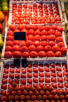Fresh, ripe tomatoes of various sizes are neatly arranged in wooden crates at a bustling local market. The bright red color catches the eye under the warm sunlight, inviting shoppers.