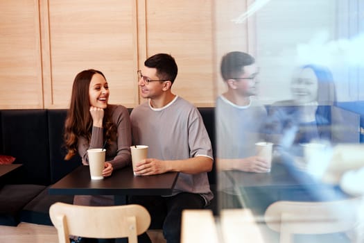 A couple shares smiles and drinks while sitting at a table in a contemporary cafe. The warm atmosphere invites relaxed conversation and connection between them.