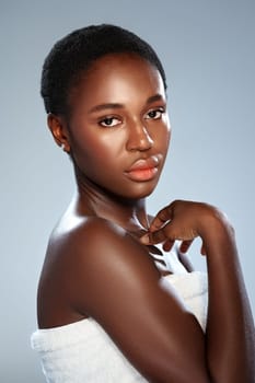 A woman with smooth skin and short hair poses gracefully while draped in a towel. Her expression is serene and confident, highlighted by soft lighting creating a serene atmosphere.