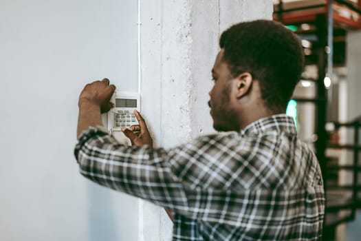 A person is adjusting a security system on a wall in a modern industrial workspace. The setting features exposed concrete and shelving in the background.