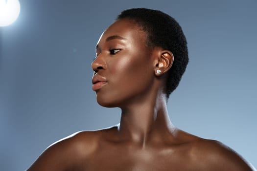 A woman with short, textured hair poses gracefully with her profile highlighted against a softly lit blue background. Her confident expression and subtle jewelry add elegance to the moment.