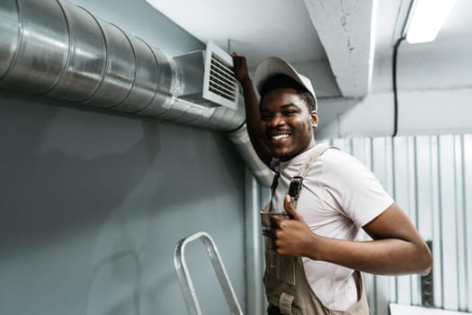 A skilled worker is installing a ventilation system in a contemporary workspace, smiling and giving a thumbs-up. The atmosphere is professional and focused on quality.