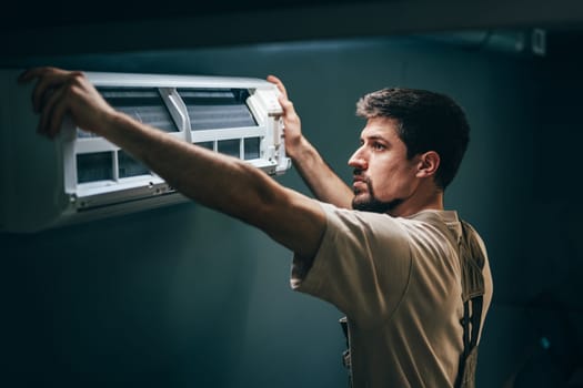 A technician carefully positions an air conditioning unit against the wall in a dimly lit room.