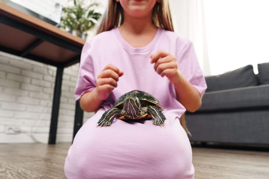 A young child enjoys their time at home, sitting on the floor with a turtle resting on their lap. The cozy living room has natural light and a relaxed atmosphere.