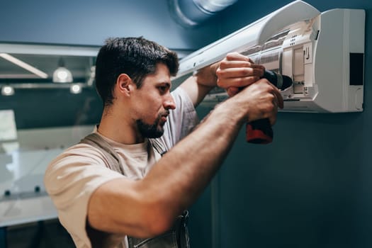 A technician is carefully installing an air conditioning unit on a wall in a modern office environment. The task requires precision and focus as he works with tools.