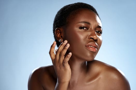 A woman with a short hairstyle stands against a light blue backdrop. She exudes confidence as she subtly touches her face, showcasing her features with a poised expression.