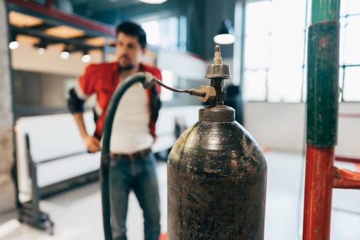 A focused worker stands behind an industrial gas cylinder, inspecting it closely in a well-lit office environment with contemporary design elements.
