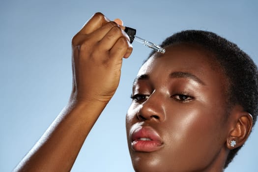 A young woman with short hair applies a skincare serum to her forehead using a dropper. Bright lighting highlights her focused expression as she takes care of her skin.