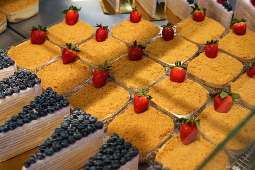 Colorful and tempting dessert selection showcases layers of cakes topped with fresh strawberries and blueberries. Perfect treat for any sweet tooth in a cozy bakery.