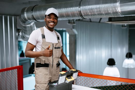 A smiling man in a work outfit stands beside a toolbox in a contemporary workspace. The environment features industrial design elements highlighting his expertise.