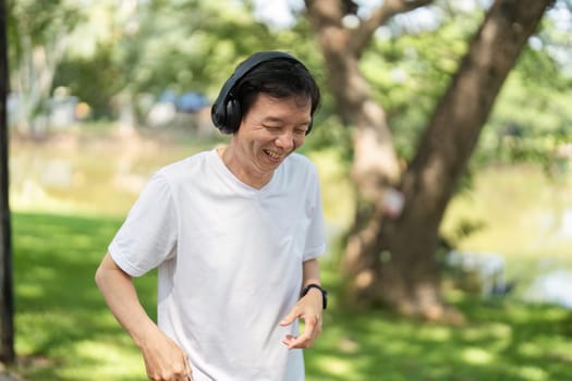 An elderly man laughs joyfully while jogging outdoors with headphones, embodying wellness and happiness in nature.
