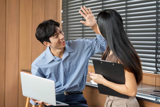Two young professionals celebrate a successful collaboration with a high-five, showcasing teamwork and positive relationships.