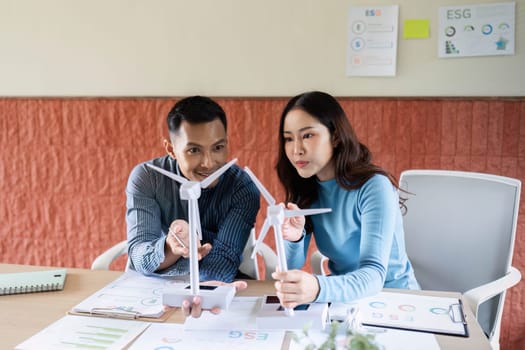 Professionals engaged in an ESG planning session, using wind turbine models to discuss renewable energy initiatives.