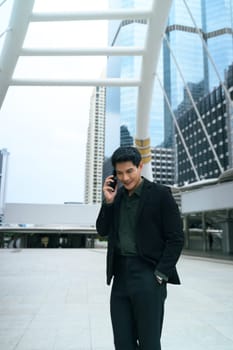 Smart businessman speaking on phone while walking through a modern cityscape.