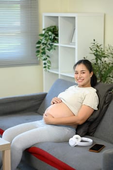 Smiling expectant mother resting on the sofa and gently holding her belly.