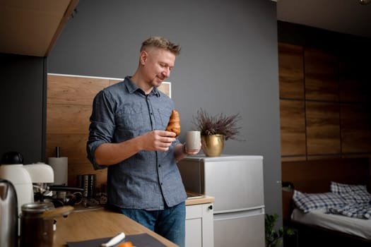 Man Having Coffee And A Croissant For Breakfast At Home In The Kitchen