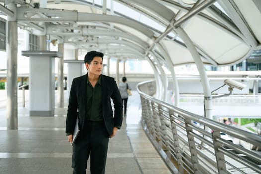 Confident businessman in a suit walking in an urban skywalk.