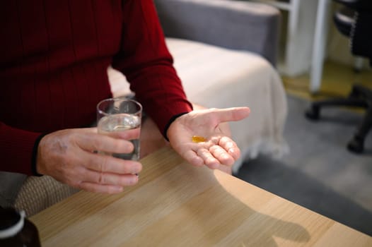 Close up of an elderly man holding a glass of water and pill.