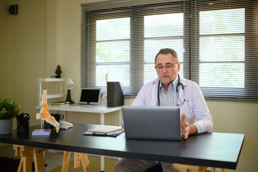 Elderly male doctor communicates through a video call, representing digital healthcare.
