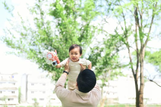Father lifts his toddler joyfully into the air on a sunny day.