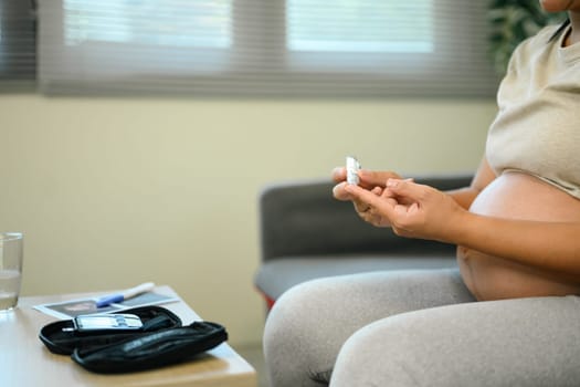 Close up of pregnant woman checking her blood sugar at home.