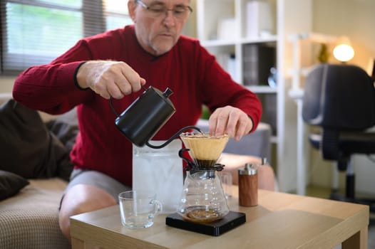 Senior man making fresh pour over coffee at home using a gooseneck kettle and glass dripper.