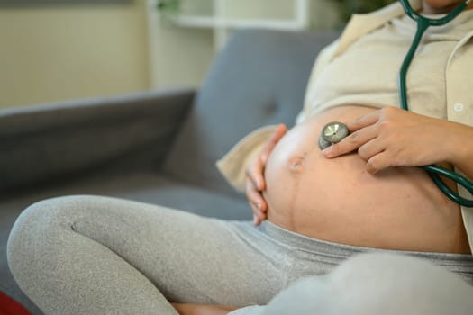 Pregnant woman listening to her baby heartbeat using a stethoscope.