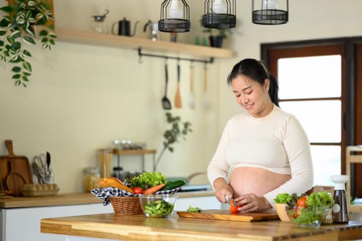 Happy pregnant woman prepares a healthy salad at home.