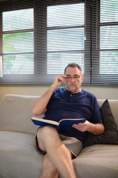 Relaxed older adult reading with concentration in a living room.