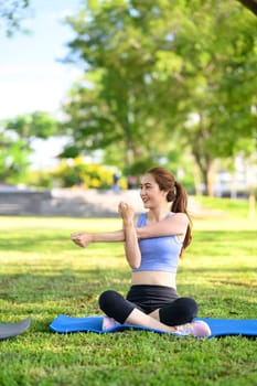 Smiling woman in workout clothes warms up for exercise on a grassy field.