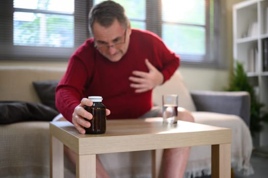 Elderly man clutching his chest while reaching for medicine. Elderly health risk concept.