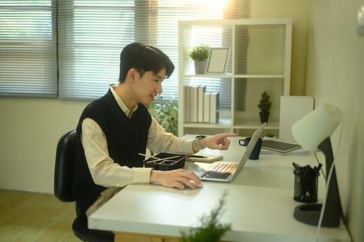 Smiling man eating instant noodles while working at his desk in a cozy, sunlit home office.