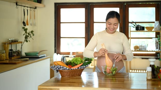 Happy pregnant woman prepares a healthy salad at home.