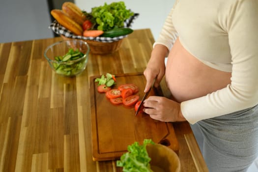 Happy pregnant woman prepares a healthy salad at home.