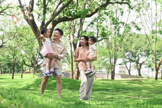 Father and mother holding their kids walk through a scenic park.