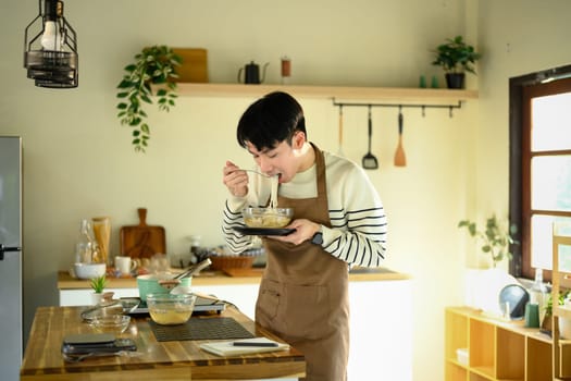 Happy asian man enjoying freshly prepared lunch in cozy kitchen.