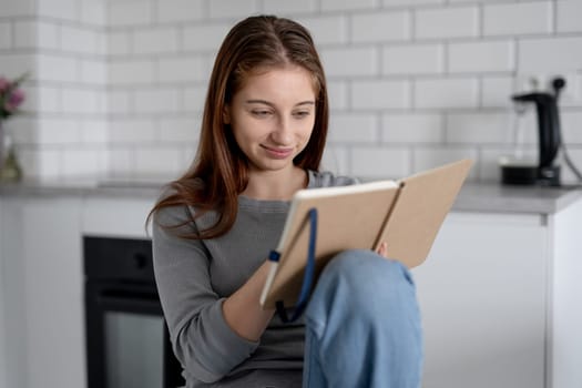 Sweet Teen Girl Reading Notebook Entries While Sitting On A Chair At Home
